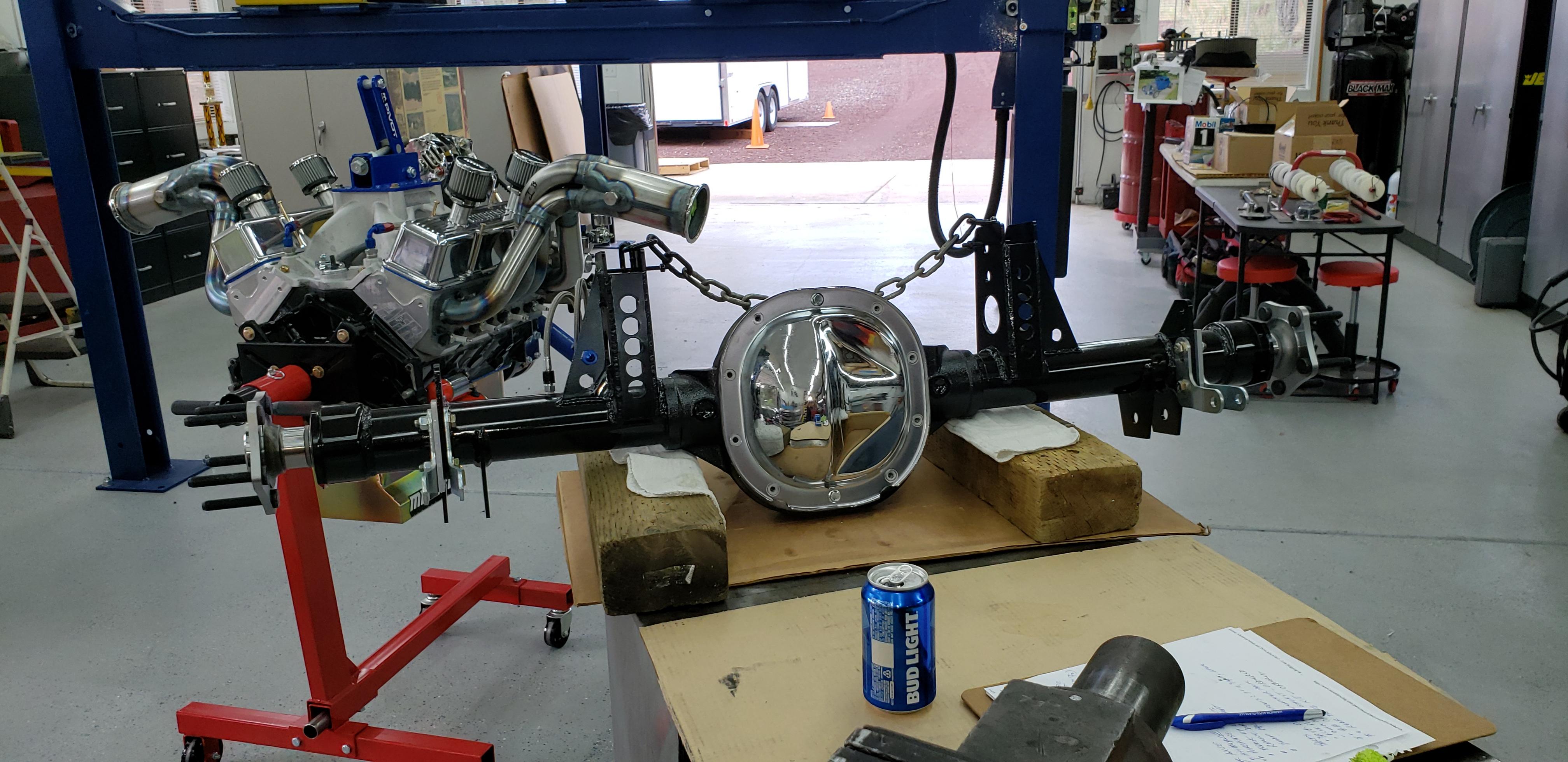 RIGHT CLICK THEN CLICK VIEW IMAGE 

Switching gears while waiting on parts.  

More power means an upgrade for the rear axle, or in this case, a complete new M88 custom axle.  I wanted to narrow the existing axle and add new style Big Ford bearing ends so it was only a little more to purchase a Moser Engineering M88 with all the mods I wanted to make to my original axle.  The M88 center section is supposed to be stronger than the Ford OEM of the existing axle and keeping the existing axle complete gives me an opportunity to sell it to offset the cost of the new.  Old axle has 31-spline Moser axles and a Detroit TruTrac LSD that worked fine with the old engine but they are not rated for the amount of power the new engine will produce.

The new axle is 5" narrower and uses Moser's pro 35-spline axle shafts and spool, the pinion is centered, uses a forged chrome moly 1350 yoke, and the large Ford style ball bearings.  This assembly is lighter and with less drag than a 9".  The axles are rated at a combined 19,200 lb ft of torque and the new engine is capable of applying 15,717 lb ft of torque to the rear axles with the 3.90:1 gear ratio.

Had to fab new brackets for the four-link and coilovers.  I'll swap the custom rear cover from the old axle as it is part of the watts link system.