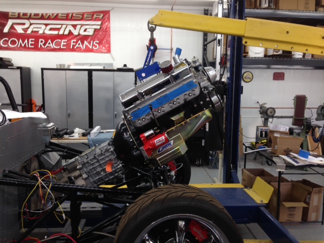 Past the 3000-hr mark on this build.  If I recall, it's supposed to take around 300-hrs to assemble the kit version (less body & paint).  I'm expecting at least another 250-hrs to go.  

Installing the engine from the front is a one-man job.  I used Weather Pack connectors for all the electrical on the grill / radiator assembly so it's easy to remove.   I run the car on the lift and elevate it high enough to get the cherry picker legs under the ramps.  Then lift the engine with the cherry picker and position it on centerline and a few feet from the end of the lift ramps.  Now I simply roll the car back and forth while lowering and tilting the engine until it's home.