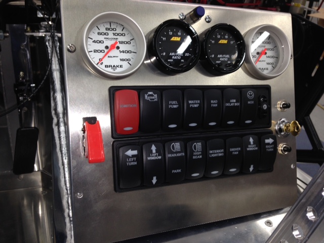 Switch & gauge panel is complete but not installed.  Ran out of switch connector plugs for the rocker switches.  A few loose ends to take care of and on to testing all circuits.  

There are 20-switches and a dimmer on this panel; 2-more for the line lock & delay box to be installed still; a master switch at the rear near the battery (NHRA requirement); fuel pump inertia switch; and 4-mechanical switches actuated by the following: the brake pedal (brake lights), 1st gear (nitrous oxide disable), low oil pressure ignition cutoff switch, and a WOT throttle switch to enable the nitrous system only at WOT.  

A lot of switches for such a simple electrical system.  I had the rocker switch actuators (covers) custom made with a description of what it operates and some have custom designs as well, such as the happy face on the arm switch for the nitrous system.  The switches are back lit with blue LEDs and some have LED indicators (oval lens at bottom) showing when they are powered up.  With so many switches I went with the back lit rocker type as I like the look better than rows of toggle switches like some of the older aircraft I used to fly.  Those old aircraft required overhead lighting for the switch panels which is not practical in this car.