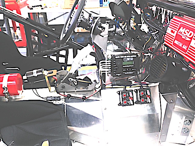 Shot of the shifter, the shift controller, and the dual 2-step rev limiters.  The trans is a manual shift auto based on the old Powerglide 2-speed and special built for drag racing.  The trans is rated for 1000 HP applications and set-up for a "full tree".  The shifter has an electrical actuator to move the gear selector and is controlled by the shift computer to shift based on time or RPM.  Most use a time based shift which can be setup to maintain your dial in number and prevent break-out.  The 2-step rev limiters are used for controlling the RPM during burnouts (4700) and for the launch (3500).  Once you stage the car you simply hold the trans brake button and floor the throttle.  The RPM is held to a pre-set limit by the launch 2-step.  When the trans brake is released the car launches at full throttle and the only rev limit is on the high end just above the shift point (6600).

The shift controller records the shift time / RPM for playback and is one more tool used to dial-in the car's performance.